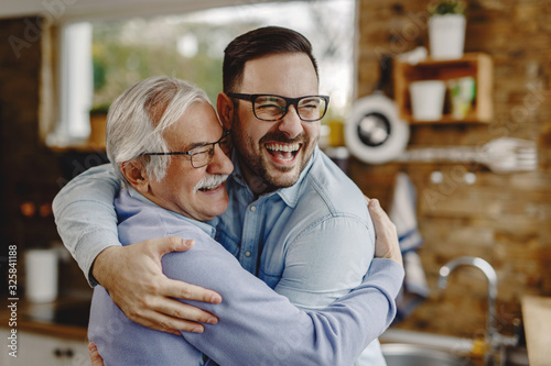 Cheerful man and his senior father embracing while greeting in the kitchen. photo
