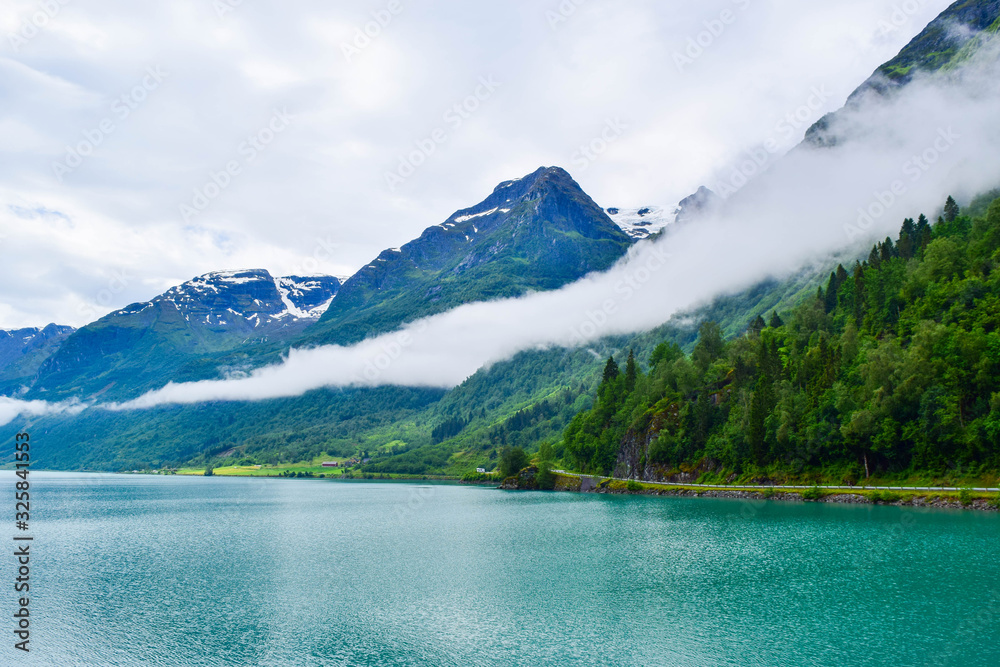 Obraz premium Landscape of beautiful Oldevatnet glacial lake and foggy mountains in which there are glaciers of Jostedalsbreen National Park. Norway.