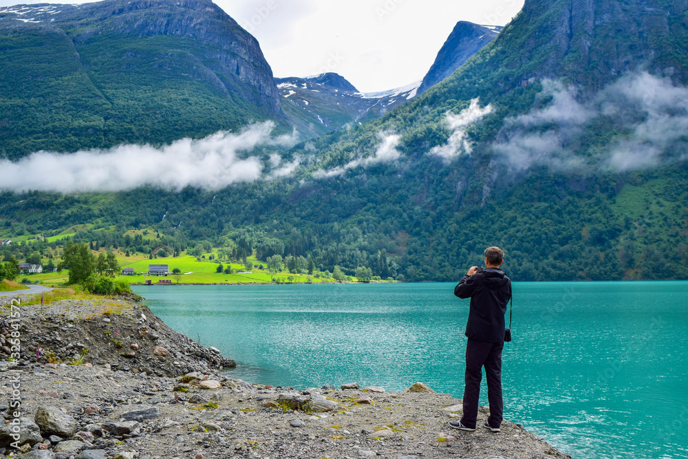 The man is taking pictures beautiful landscape of Oldevatnet glacial lake and foggy mountains. Norway.