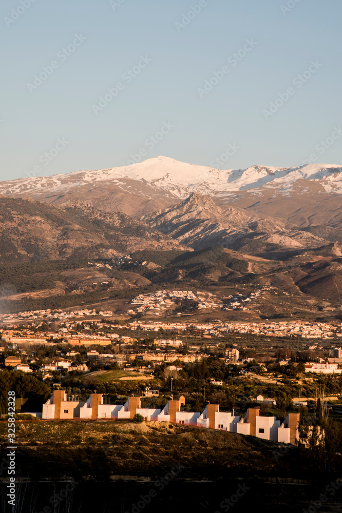 landscape with snowy mountains and valley with houses at sunset