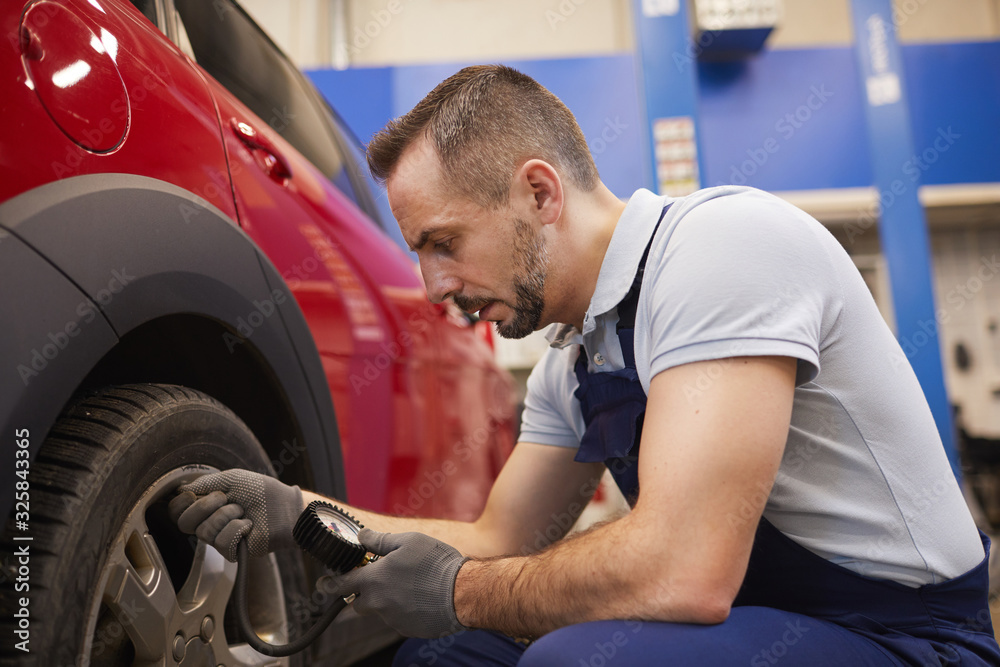 Side view portrait of bearded car mechanic checking pressure in tires during vehicle inspection in garage shop, copy space Side view portrait of bearded car mechanic checking pressure in tires during vehicle inspection in garage shop, copy space