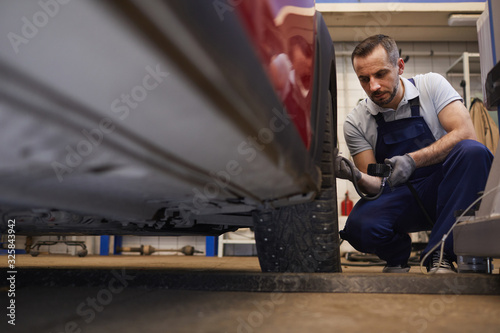 Low angle portrait of bearded car mechanic checking pressure in tires during vehicle inspection in garage shop, copy space
