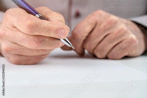 pensioner holds pen above blank paper on white table