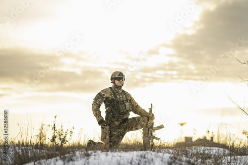 Modern soldier in the winter desert put gun on the ground and knelt down. full equipment commandos with helmet and weapon. atmosphere after moder special force battle