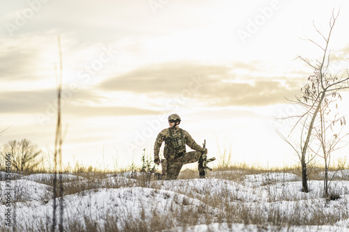 Modern soldier in the winter desert put gun on the ground and knelt down. full equipment commandos with helmet and weapon. atmosphere after moder special force battle