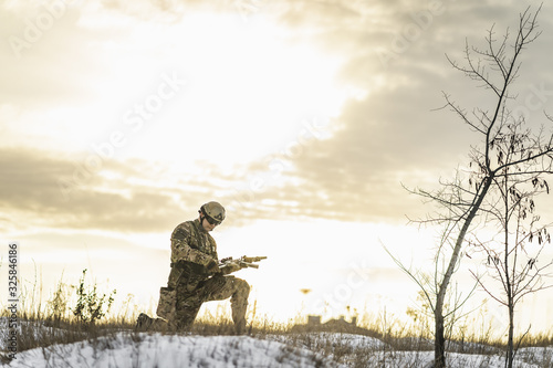 Modern war soldier army Man in the winter desert put gun on the ground and knelt down. full equipment commandos with helmet and weapon . atmosphere after moder special force battle
