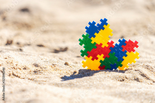 Autism friendly holidays. Colorful autism awareness heart on sunny beach sand