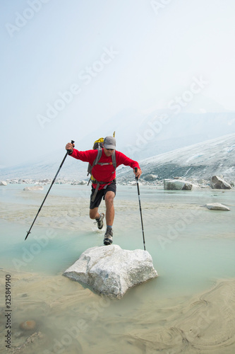 Backpacker leaps over stream onto boulder near glacier. photo