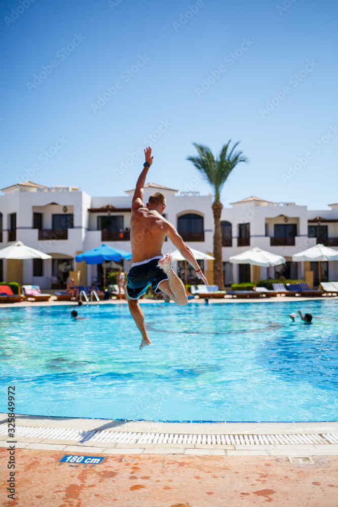 Guy in shorts bathes in the pool under the bright sun