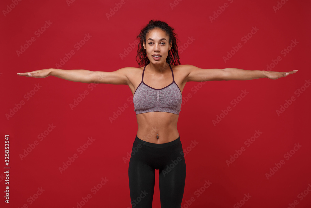 Beautiful young african american sports fitness woman in sportswear posing working out isolated on red background in studio. Sport exercises healthy lifestyle concept. Spreading outstretched hands. Beautiful young african american sports fitness woman in sportswear posing working out isolated on red background in studio. Sport exercises healthy lifestyle concept. Spreading outstretched hands.
