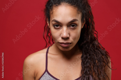 Confident young african american sports fitness woman in sportswear posing working out isolated on red wall background studio portrait. Sport exercises healthy lifestyle concept. Looking camera.