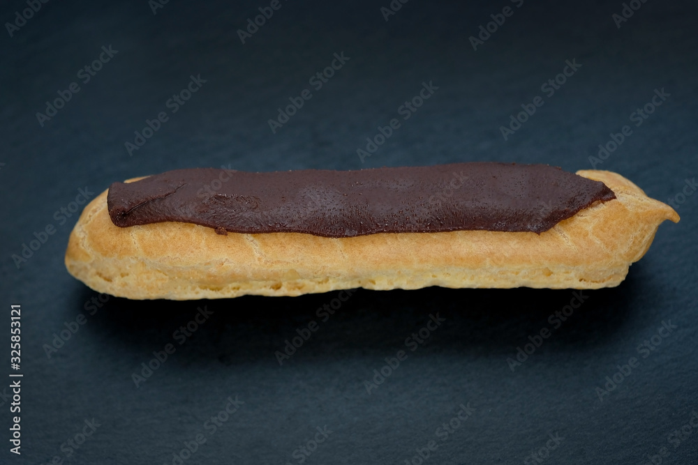 eclairs cake stuffed on a black background. homemade eclair covered with a strip of chocolate. eclairs cake stuffed on a black background. homemade eclair covered with a strip of chocolate.