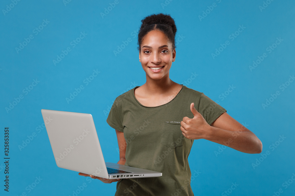 Funny young african american woman girl in casual t-shirt posing isolated on blue background studio portrait. People lifestyle concept. Mock up copy space. Hold laptop pc computer showing thumb up. Funny young african american woman girl in casual t-shirt posing isolated on blue background studio portrait. People lifestyle concept. Mock up copy space. Hold laptop pc computer showing thumb up.