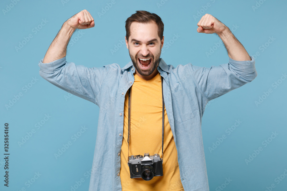 Fototapeta premium Strong traveler tourist man in yellow summer clothes with photo camera isolated on blue background. Male passenger traveling abroad on weekends. Air flight journey concept. Showing biceps, muscles.
