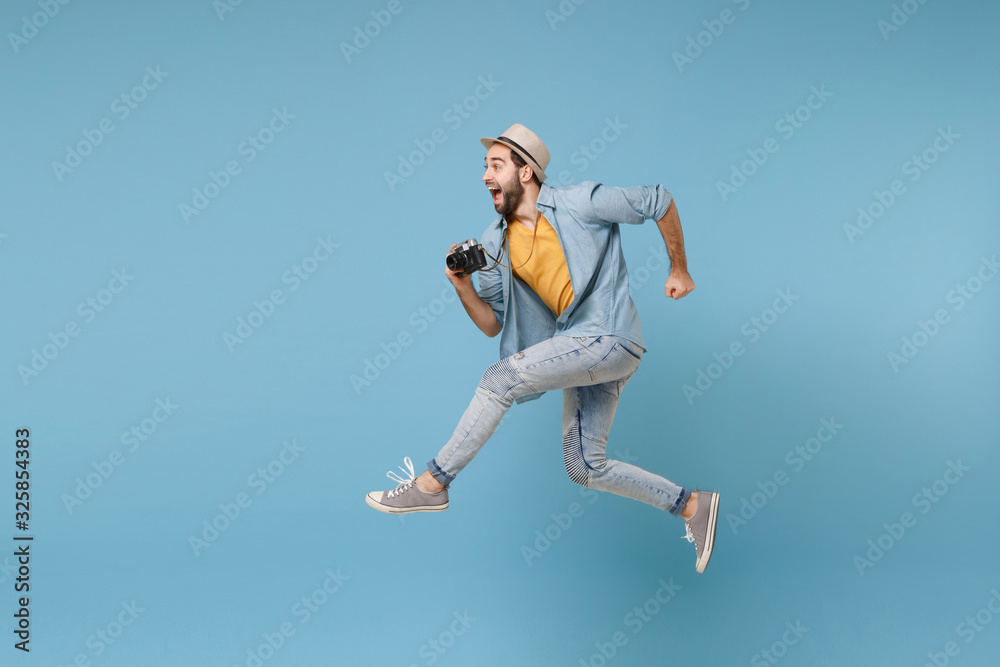 Side view of excited traveler tourist man in yellow clothes with photo camera isolated on blue background. Male passenger traveling abroad on weekend. Air flight journey concept. Jumping like running. Side view of excited traveler tourist man in yellow clothes with photo camera isolated on blue background. Male passenger traveling abroad on weekend. Air flight journey concept. Jumping like running.