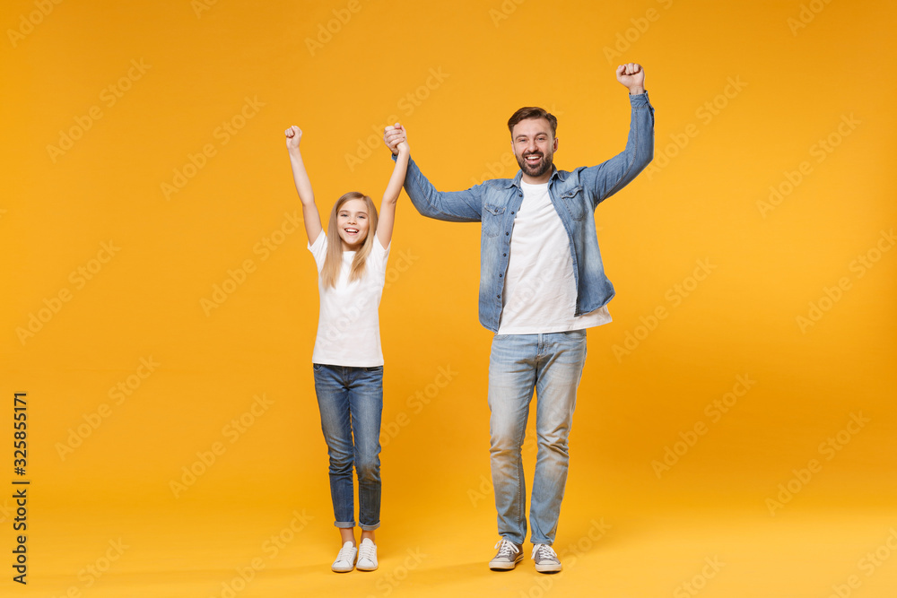 Fototapeta premium Happy bearded man in casual clothes with child baby girl. Father little kid daughter isolated on yellow background. Love family parenthood childhood concept. Rising holding hands doing winner gesture.