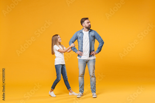 Bearded man in casual clothes with child baby girl. Father little kid daughter isolated on yellow background. Love family parenthood childhood concept. Stand with arms akimbo on waist holding hands.