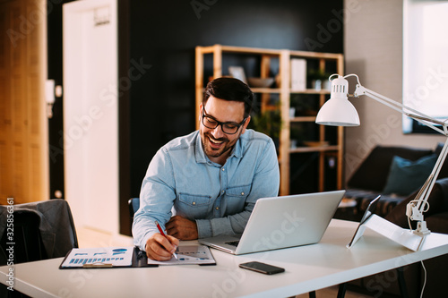 Young business man working at home with laptop and papers on desk photo