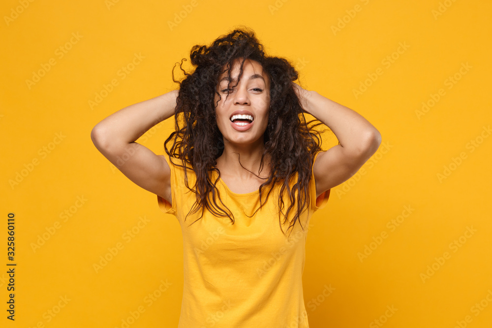 Laughing young african american woman girl in casual t-shirt posing isolated on yellow orange background in studio. People lifestyle concept. Mock up copy space. Having fun holding hands behind head. Laughing young african american woman girl in casual t-shirt posing isolated on yellow orange background in studio. People lifestyle concept. Mock up copy space. Having fun holding hands behind head.