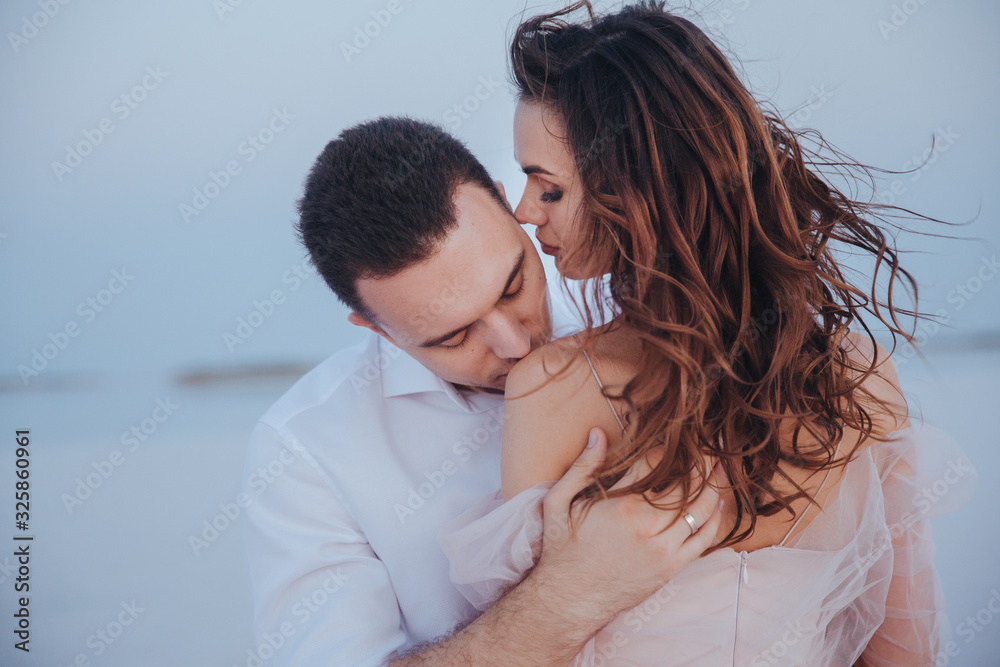 attractive newlyweds on the sea shore. Goom kissing bride's shoulder. side and back view attractive newlyweds on the sea shore. Goom kissing bride's shoulder. side and back view