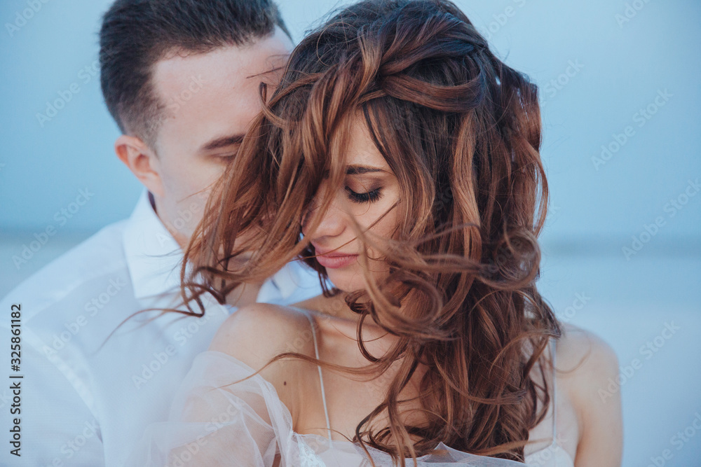 beautiful newlyweds on the sea shore and gentle groom, touching the bride and her flying hair. Front view