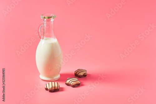 Full jug of fresh milk, yogurt or kefir near chocolate candies on pink background. Space for text