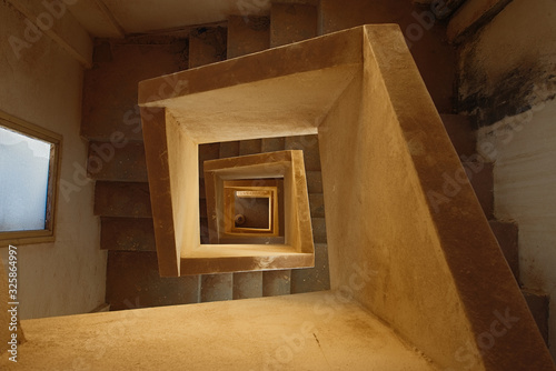 squared spiral multi-flight stairway with yellow concrete handrails seen from the top of the staircase.