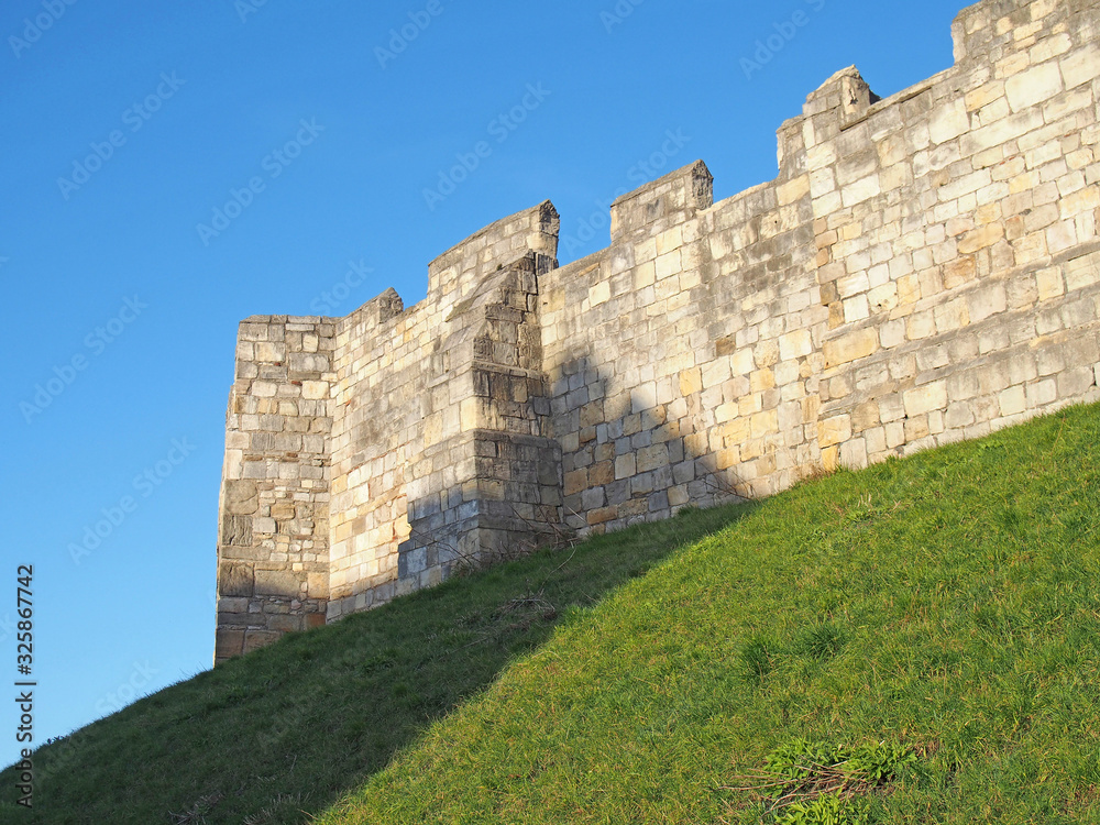 a view of the ancient medieval city walls of york with grass covered embankment and blue sky