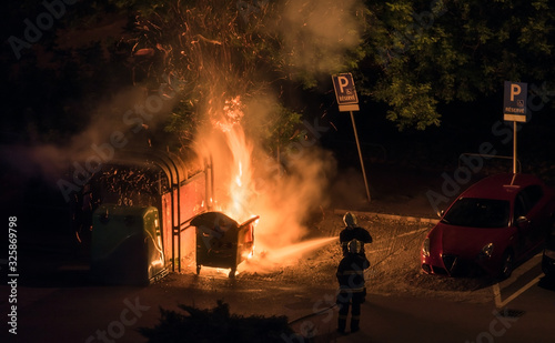 Firefighters Extinguish Burning Plastic Dumpster near Parking Lot at Night
