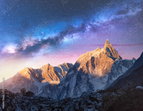 Milky Way over beautiful mountains at night in Nepal. Colorful space landscape with purple starry sky, snowy mountain peak and sunlight at sunrise. Galaxy, stars and high rocks. Travel and nature © den-belitsky