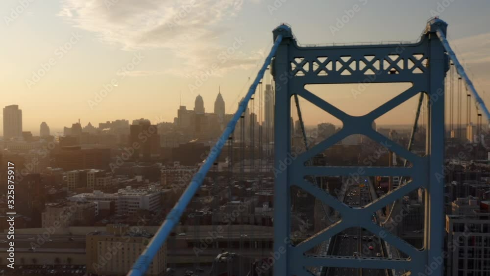 Aerial view of the Ben Franklin bridge passing in front of the Philadelphia skyline during a smoggy, warm, sunset