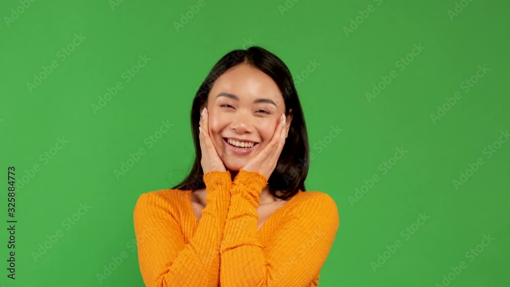 Young pretty girl of Asian appearance smiles enthusiastically opening her mouth and taking her face with both hands Young pretty girl of Asian appearance smiles enthusiastically opening her mouth and taking her face with both hands
