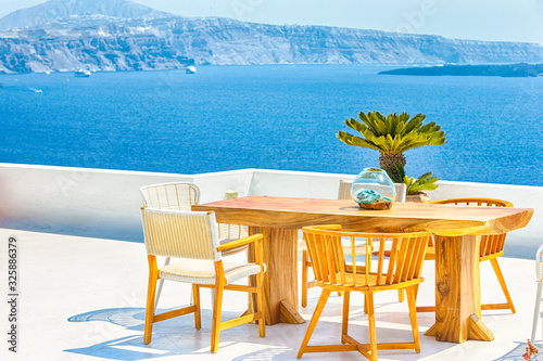 Traveling Concepts. View of Tranquil Open Air Dining Tables with Chairs as a Place of Rest and Relaxation in Oia or Ia Village at Santorini Island in Greece Against Blue Aegean Sea.
