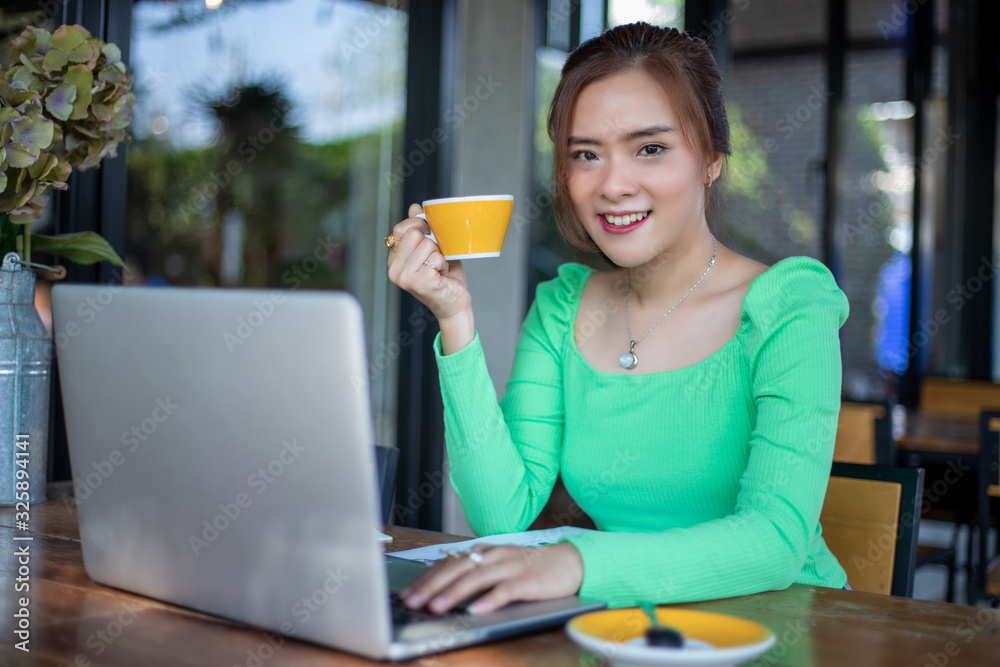 Asian businesswomen smiling and using notebook for analysis documents and graph financial diagram working and she is drinking coffee at coffee shop Asian businesswomen smiling and using notebook for analysis documents and graph financial diagram working and she is drinking coffee at coffee shop