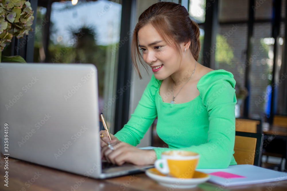 Asian businesswomen smiling and using notebook for analysis documents and graph financial diagram working and she is drinking coffee at coffee shop Asian businesswomen smiling and using notebook for analysis documents and graph financial diagram working and she is drinking coffee at coffee shop