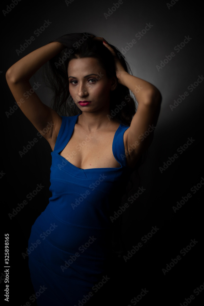 Fashion portrait of an young and attractive Indian Bengali brunette girl with blue western dress in front of a black studio background. Indian fashion portrait and lifestyle.