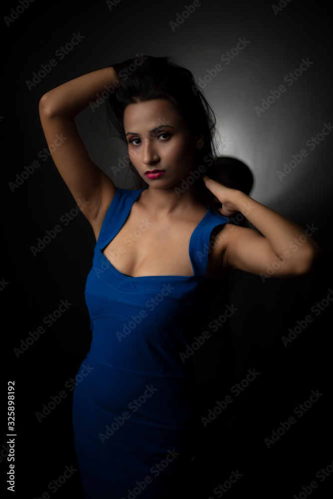 Fashion portrait of an young and attractive Indian Bengali brunette girl with blue western dress in front of a black studio background. Indian fashion portrait and lifestyle.