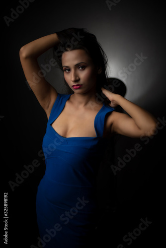 Fashion portrait of an young and attractive Indian Bengali brunette girl with blue western dress in front of a black studio background. Indian fashion portrait and lifestyle.