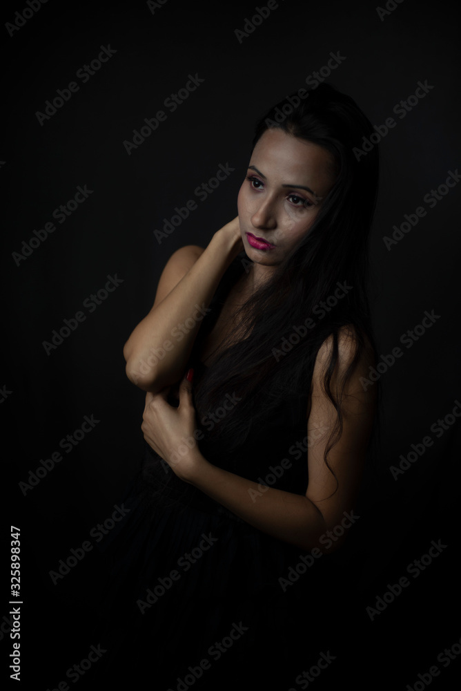 Fashion portrait of young and attractive Indian Bengali brunette girl in black western dress in front of black studio background. Indian lifestyle.