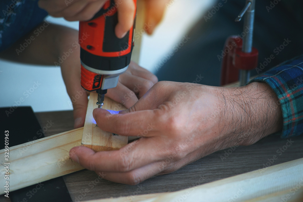 Hand boy and his father works with a screwdriver on a piece of wood Hand boy and his father works with a screwdriver on a piece of wood