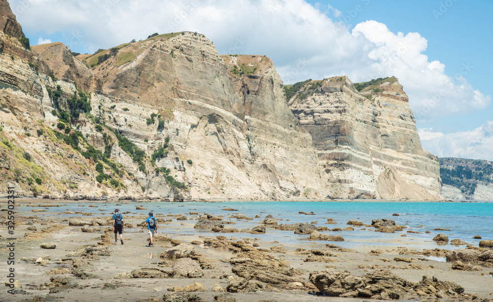 Tourist walking on the beach with beautiful geological cliff formations on the coast to Cape Kidnappers in Hawke's Bay region of New Zealand.