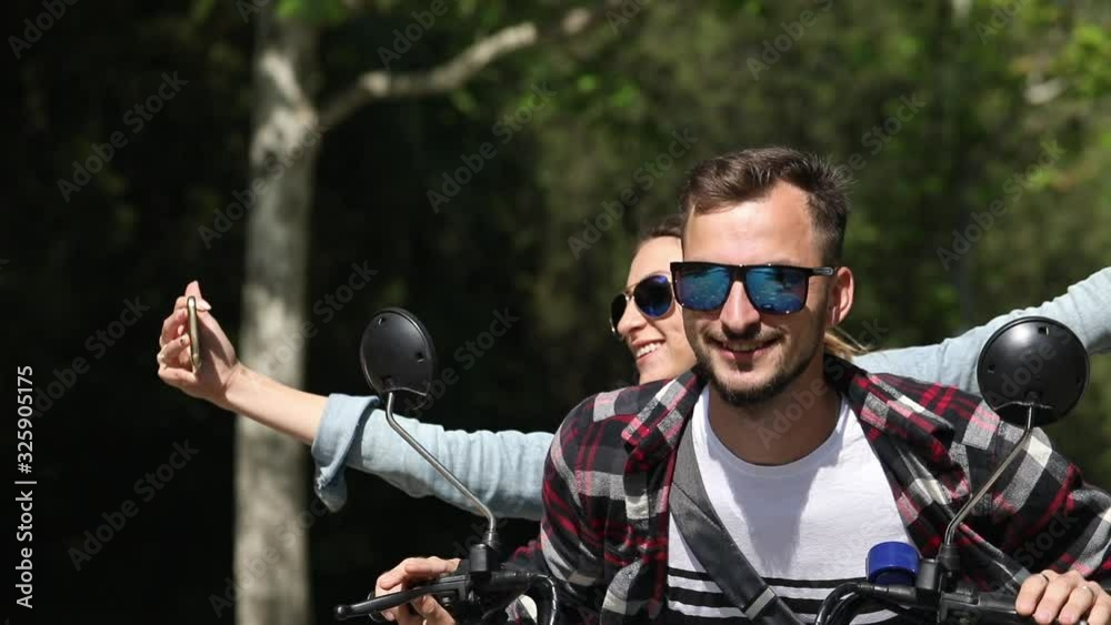Couple in love ride an electric scooter in the park and take selfie on the phone, the camera shoots them from the side. Couple in love ride an electric scooter in the park and take selfie on the phone, the camera shoots them from the side.
