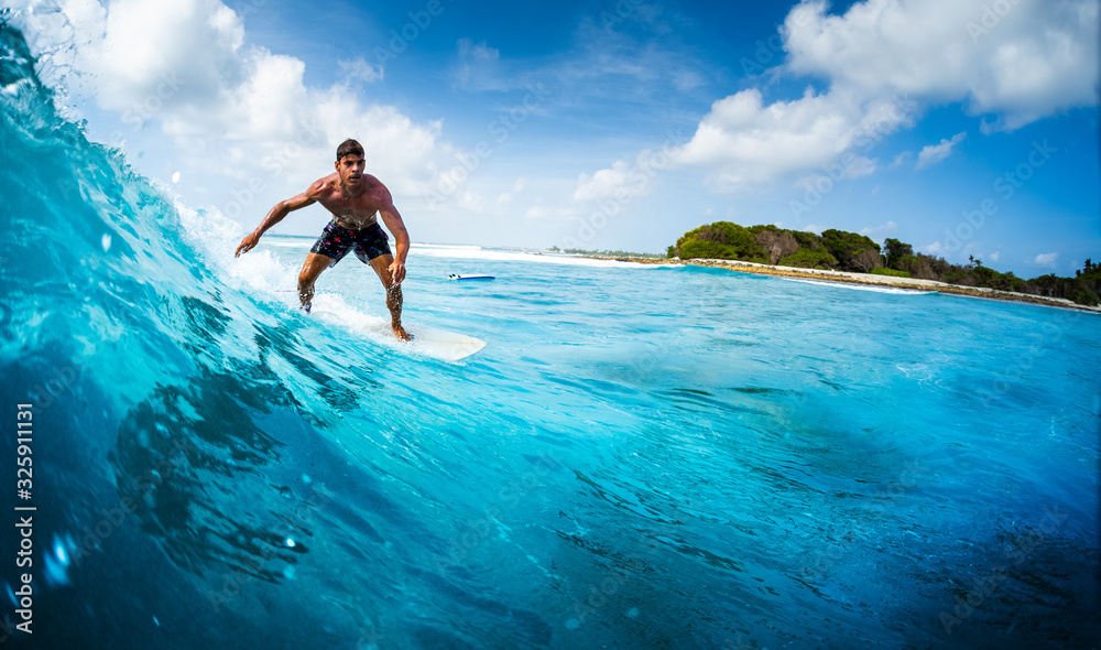 Young athletic surfer rides the ocean wave on Sultans surf spot in Maldives