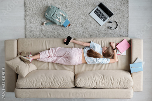 High angle view of tired teenage girl sleeping with phone in hand on sofa in living room, she resting after school