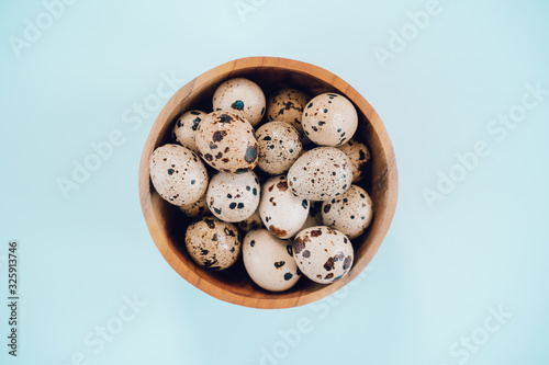 Quail eggs in wooden bowl on a blue background. Easter concept, flay lay photo. Mockup, space for text.