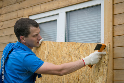 worker, boarded up the window of the house with a protective shield made of wood, from thieves, when moving to another address, close-up