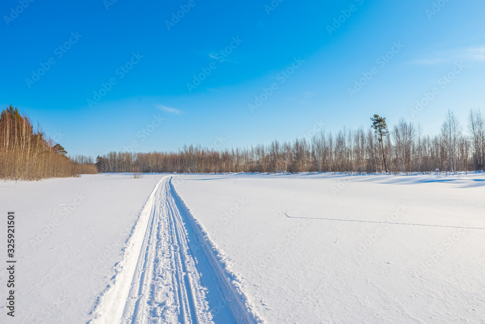 Snowmobile road on a snowy field. Winter landscape on a bright sunny day Snowmobile road on a snowy field. Winter landscape on a bright sunny day