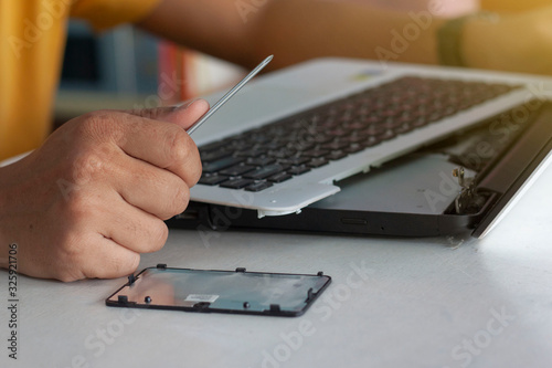 The hand of the mechanic is holding a screwdriver to fix the laptop computer.