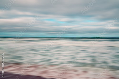 Abstract  seascape with blurred panning motion. Overcast day, ocean waves, and cloudy sky. Image displays blue and light pink split-toned color scheme. © Hanna Tor