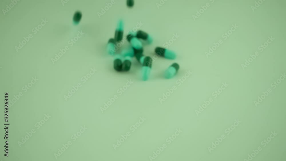 Capsules of medicine falling on green background in slow motion Capsules of medicine falling on green background in slow motion